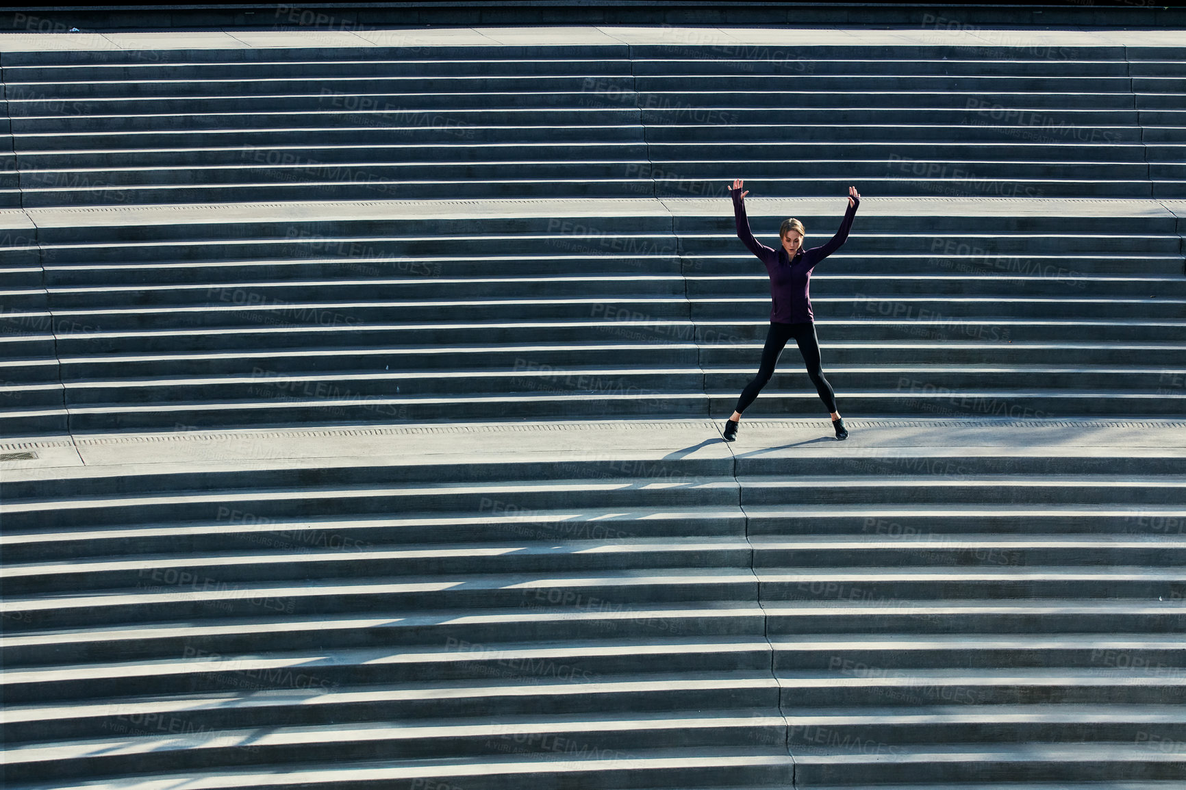 Buy stock photo High angle shot of an attractive young sportswoman doing jumping jacks on outside stairs