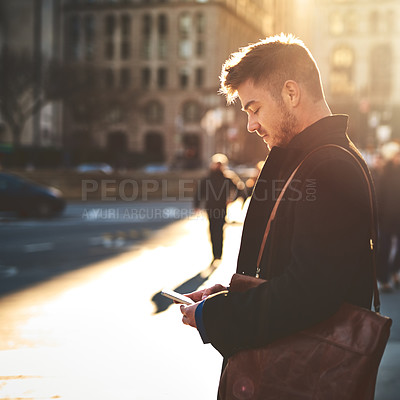 Buy stock photo Shot of a focused young man texting on his phone while standing in the busy streets of the city on his way to work