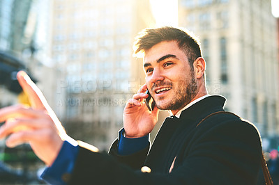 Buy stock photo Shot of a cheerful young man talking on his phone while waiting for a taxi to take him to work in the morning