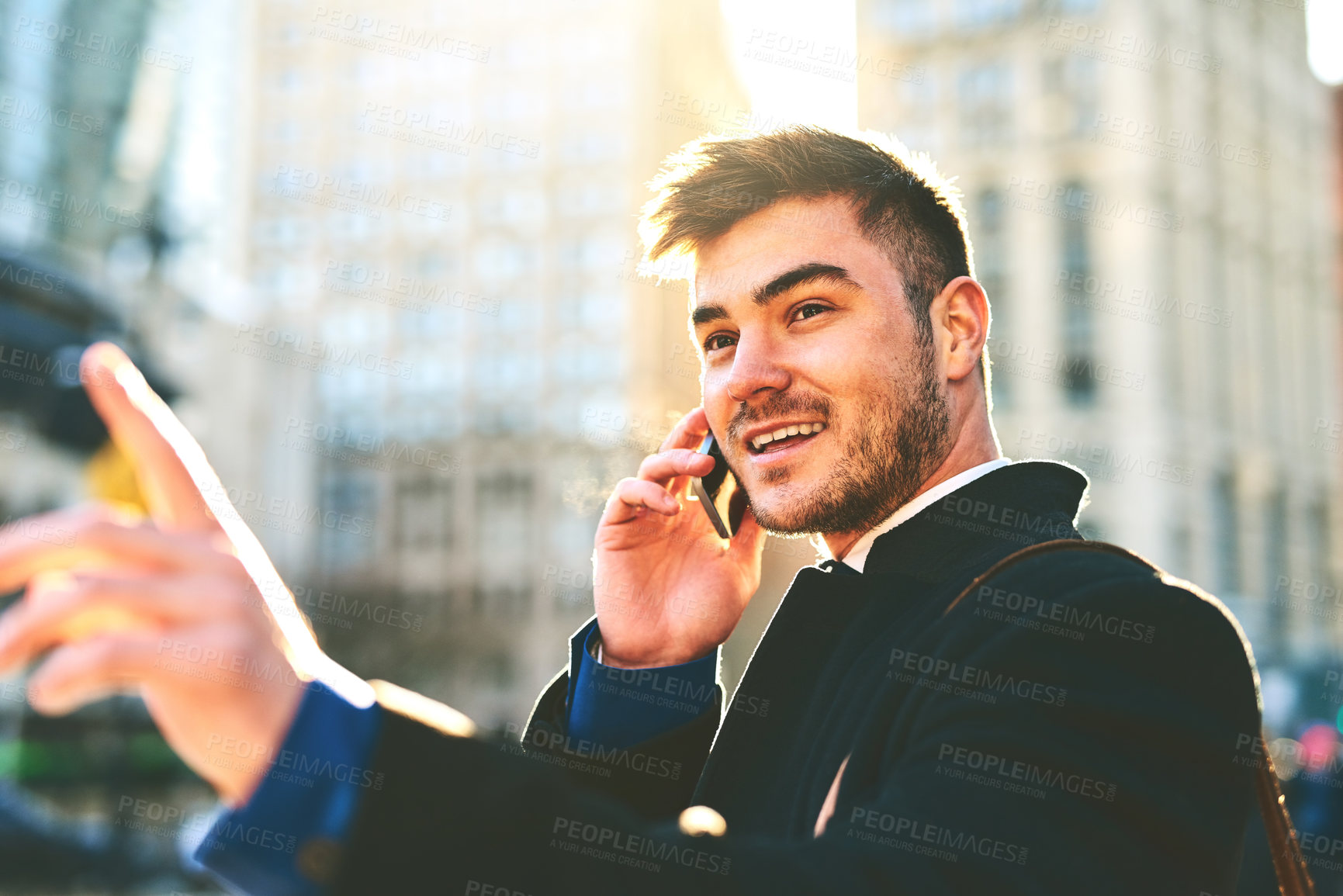 Buy stock photo Shot of a cheerful young man talking on his phone while waiting for a taxi to take him to work in the morning