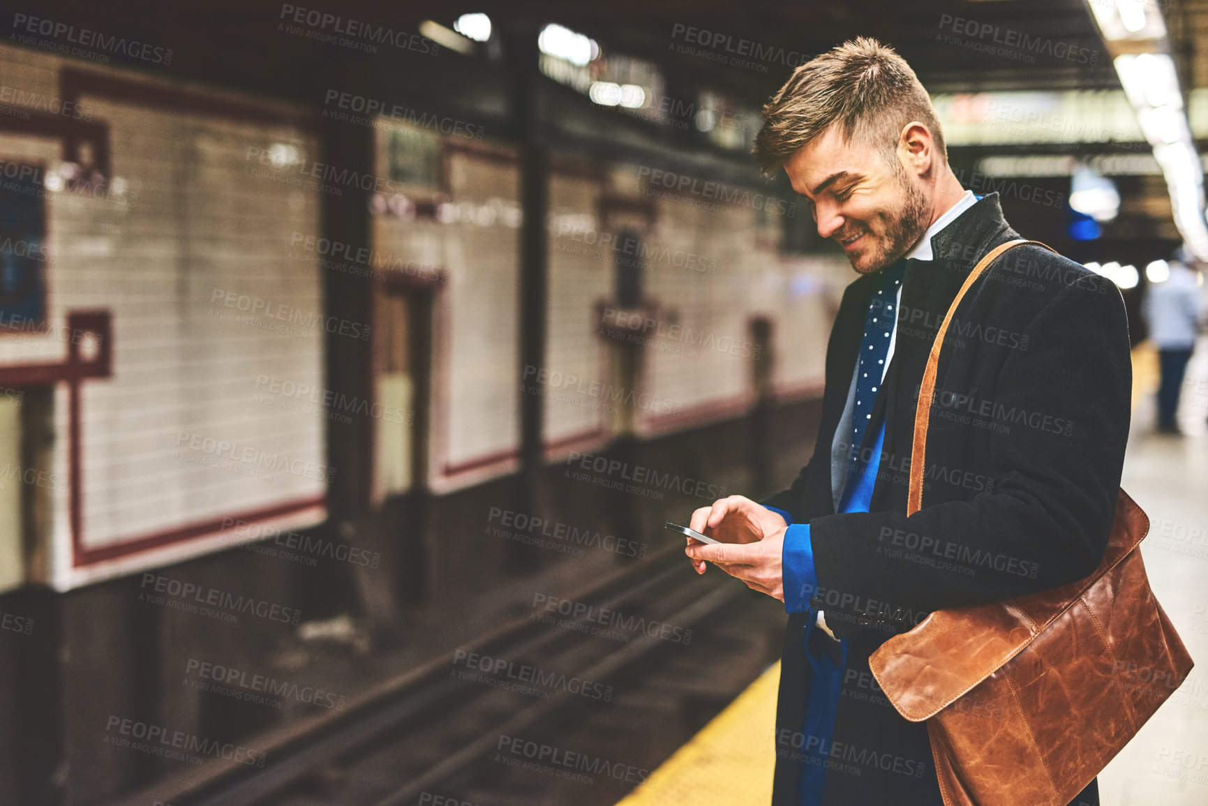 Buy stock photo Shot of a cheerful young man texting on his phone while waiting for a train to take him to work in the morning