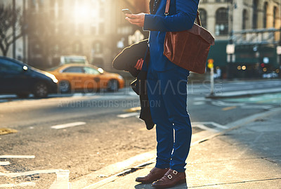 Buy stock photo Low angle shot of a unrecognizable man texting on his phone while waiting for a taxi to take him to work in the morning