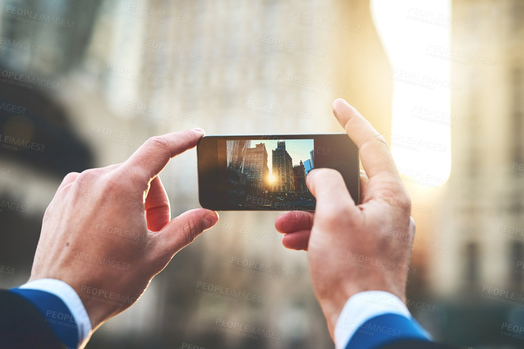 Buy stock photo Shot of an unrecognizable man taking a picture of the sun rising over buildings in the city during the morning hours
