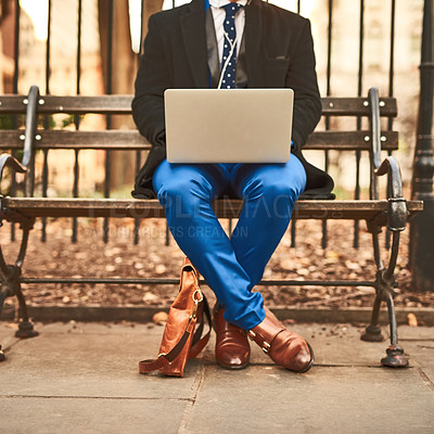 Buy stock photo Shot of an unrecognizable man working on his laptop while being seated on a bench outside during the day