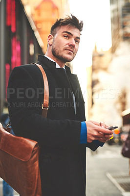 Buy stock photo Shot of a young well dressed man texting on his cellphone while waiting for a taxi to get him to work in the morning
