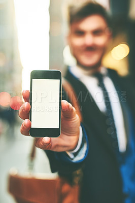 Buy stock photo Closeup of a cheerful young man holding up a cellphone and showing the screen to the camera outside in the city during the day