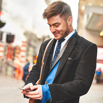 Buy stock photo Shot of a young well dressed man texting on his cellphone while waiting for a taxi to get him to work in the morning