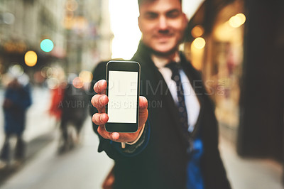 Buy stock photo Closeup of a cheerful young man holding up a cellphone and showing the screen to the camera outside in the city during the day