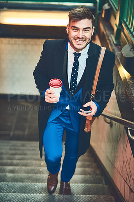Buy stock photo Portrait of a cheerful young businessman texting on his phone and drinking coffee while walking up a flight of stairs in a subway during the morning hours