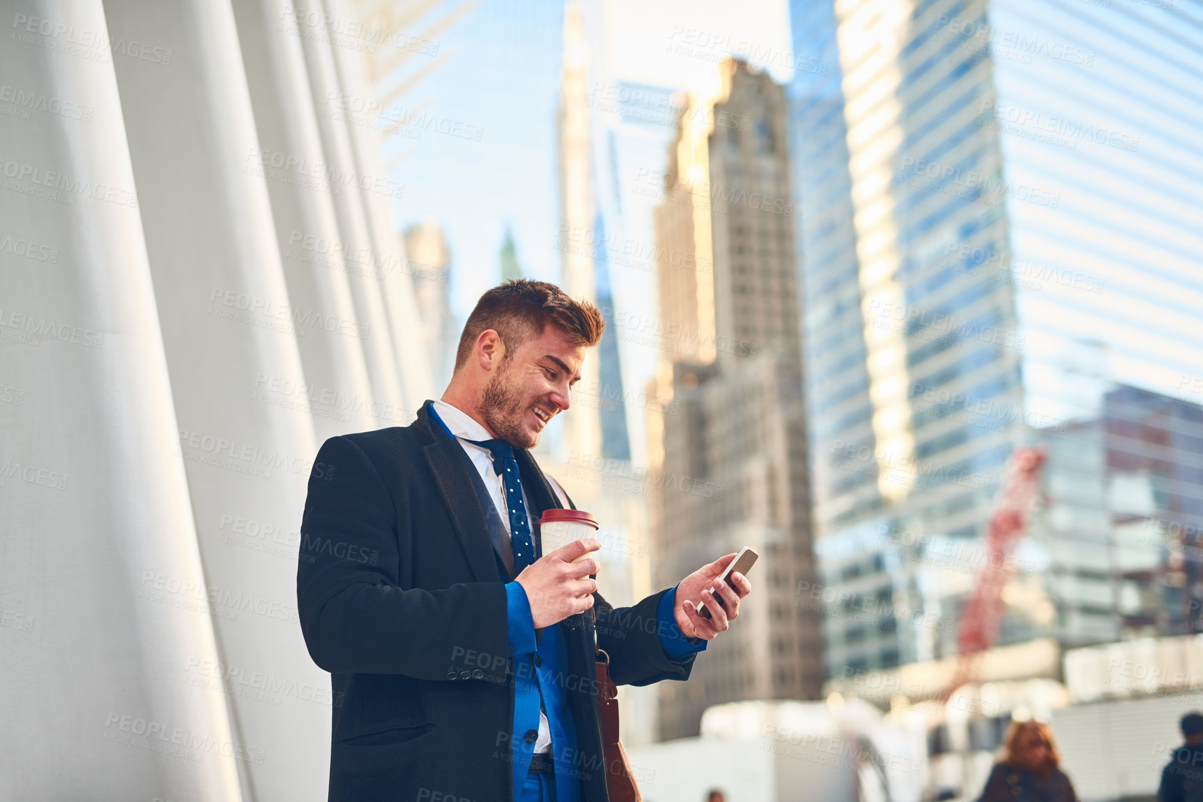 Buy stock photo Shot of a cheerful young man texting on his phone while drinking coffee at work during the morning hours