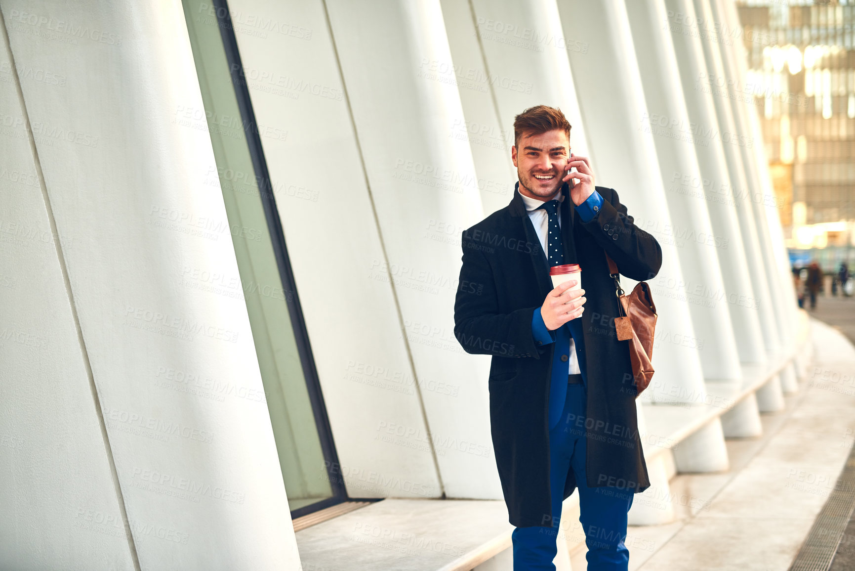Buy stock photo Portrait of a cheerful young man talking on his phone while drinking coffee at work during the morning hours