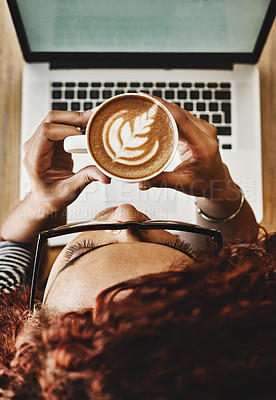 Buy stock photo High angle shot of a young woman drinking coffee while working on a laptop in a cafe