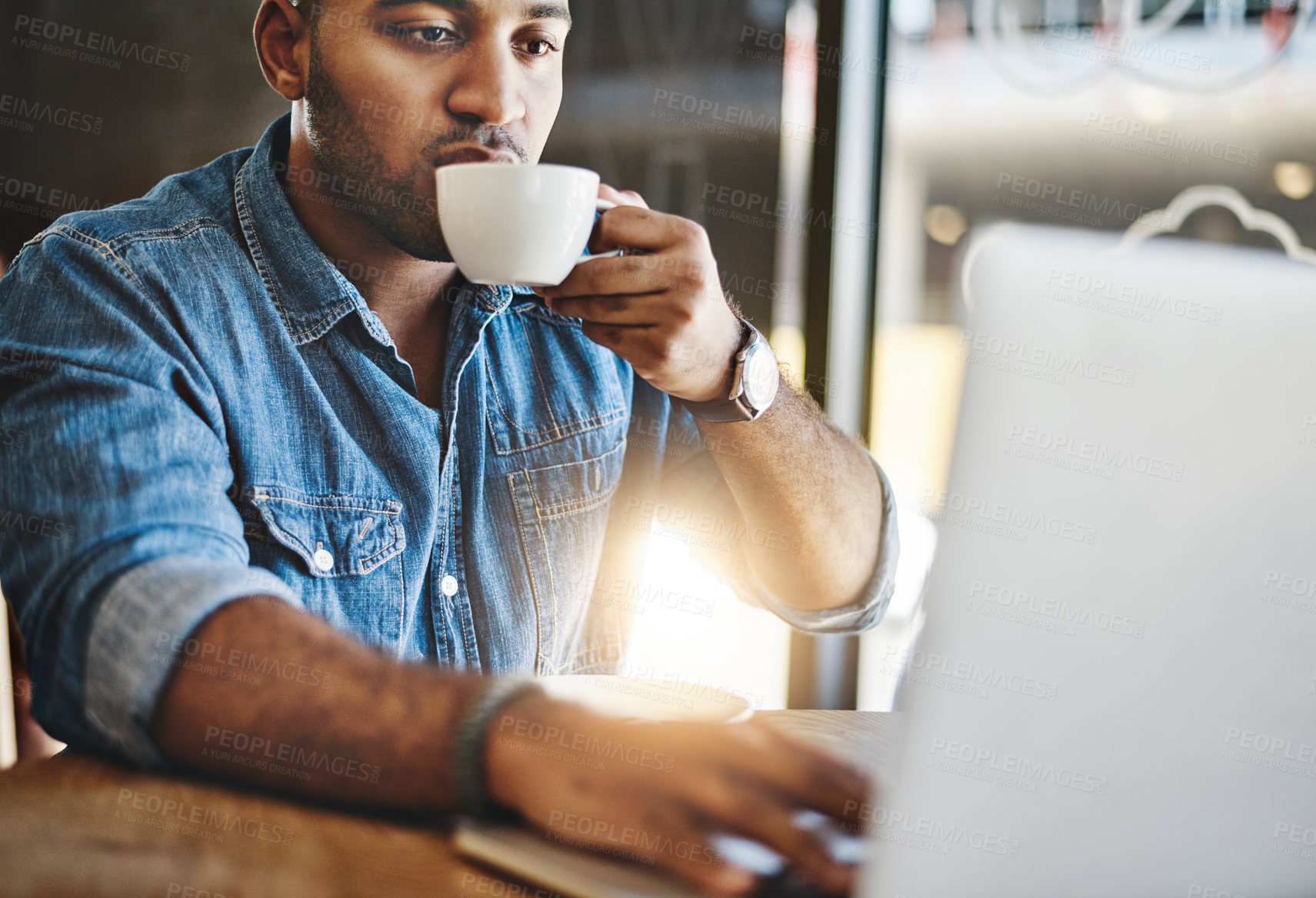 Buy stock photo Shot of a handsome young man drinking coffee while working working in a cafe