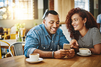 Buy stock photo Cropped shot of an affectionate young couple looking at a cellphone while sitting in a coffee shop