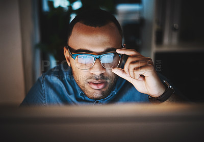 Buy stock photo Shot of a young businessman using a computer during a late night at work in a modern office