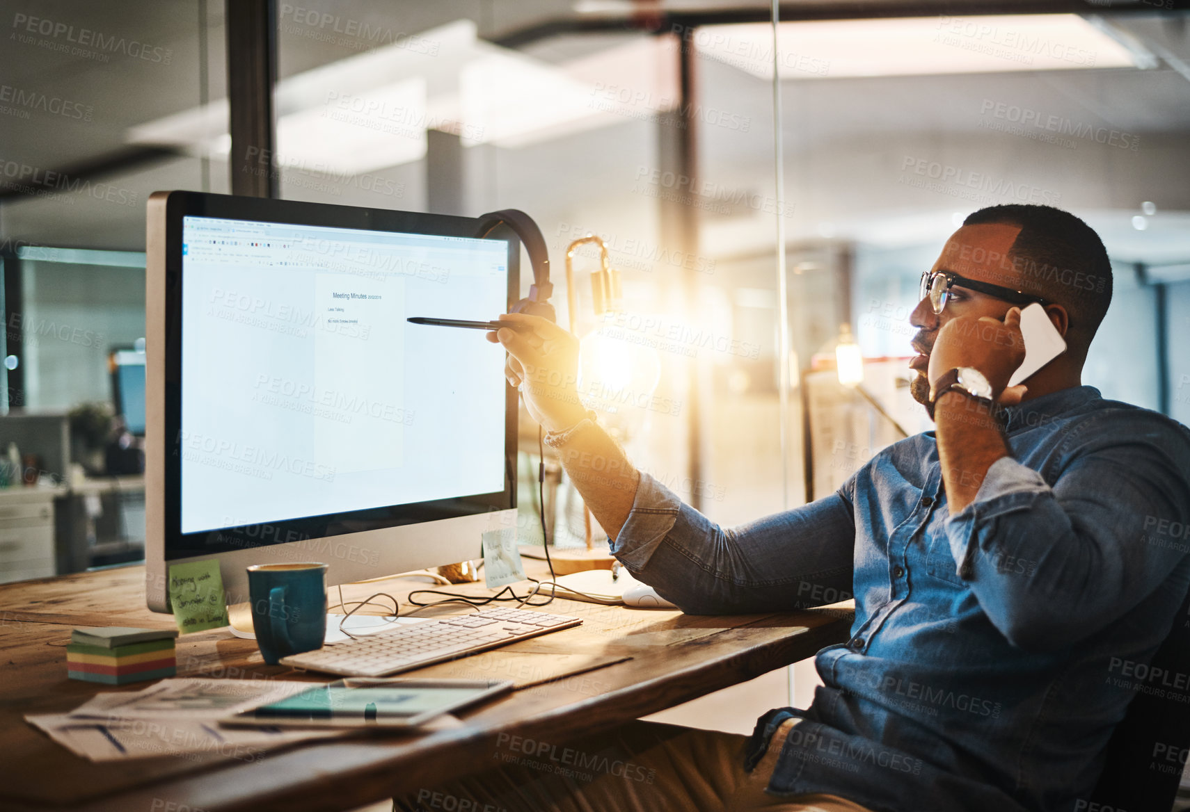 Buy stock photo Shot of a young businessman talking on his phone and using a computer during a late night at work