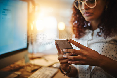 Buy stock photo Cropped shot of a young businesswoman using a mobile phone during a late night at work