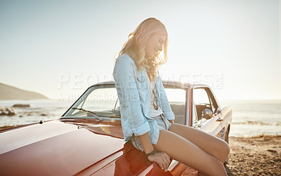 Buy stock photo Shot of a beautiful young woman relaxing on the hood of her car on a road trip