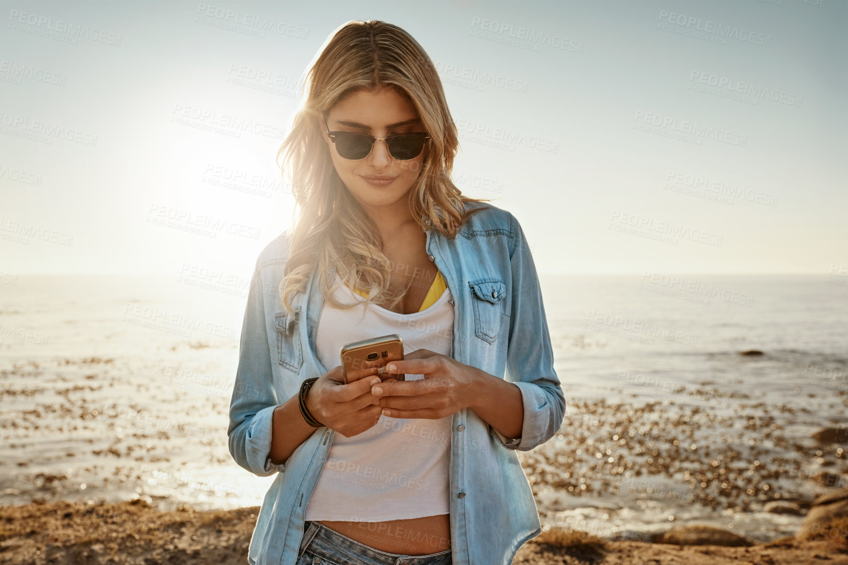 Buy stock photo Shot of a beautiful young woman using a mobile phone at the beach