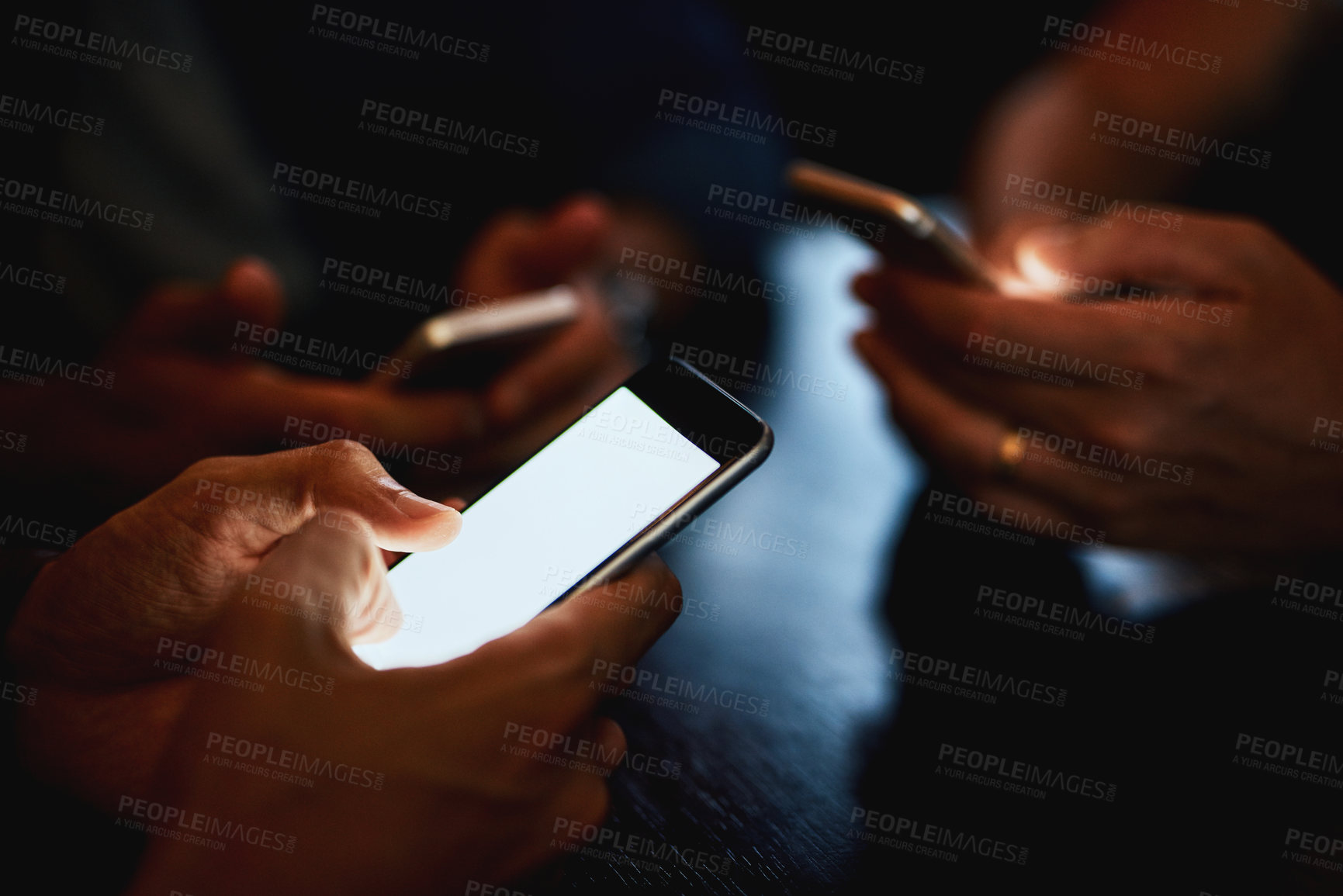 Buy stock photo Closeup of a group of unrecognizable people texting on their phones while being seated inside of a bar at night