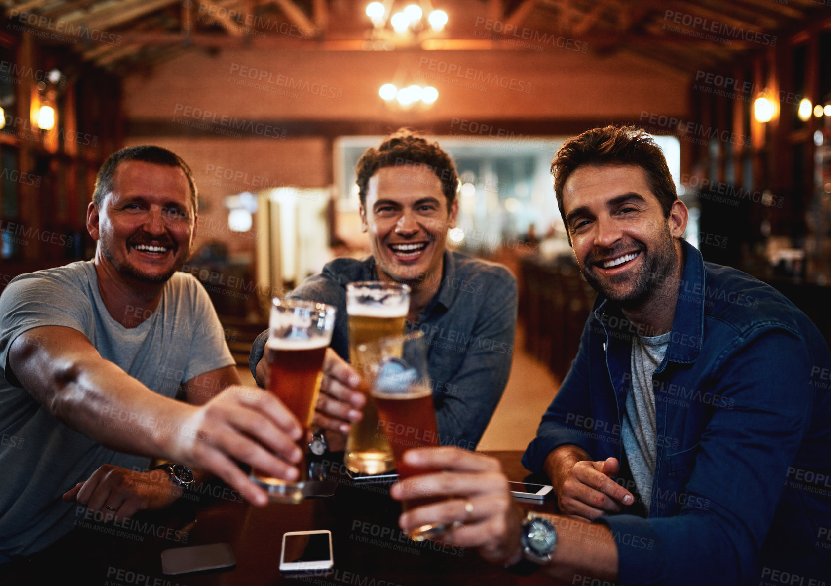 Buy stock photo Portrait of a group of young friends seated at a table together while enjoying a beer and celebrating with a celebratory toast inside a bar