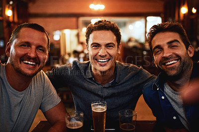 Buy stock photo Portrait of a cheerful young group of friends having beers together while being seated at a table inside a bar at night