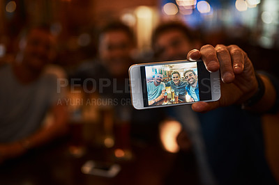 Buy stock photo Closeup of a group of cheerful young friends taking a self portrait together while enjoying beer together at a bar during the night