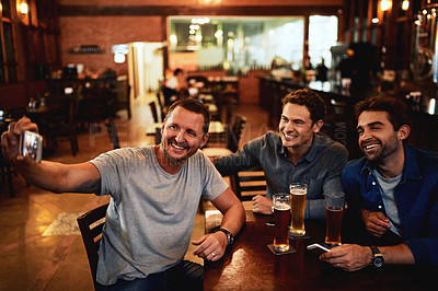Buy stock photo Shot of a group of cheerful young friends taking a self portrait together while enjoying beer together at a bar during the night