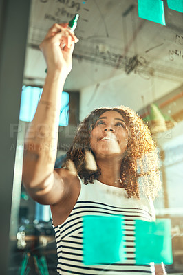 Buy stock photo Shot of a focussed young businesswoman putting up sticky notes on a glass wall while brainstorming in the office at work