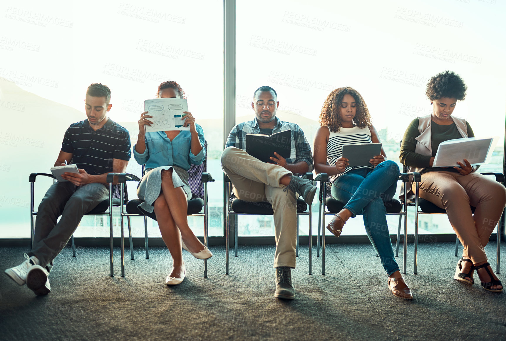 Buy stock photo Shot of a group of young focussed work colleagues seated on chairs next to each other in a row while making notes inside of the office during the day