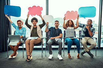 Buy stock photo Portrait of a cheerful young group of work colleagues seated next to each other while holding up signs inside of the office during the day