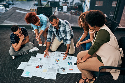 Buy stock photo Shot of a group of focussed young coworkers working together and brainstorming while being seated on the floor of the office at work during the day