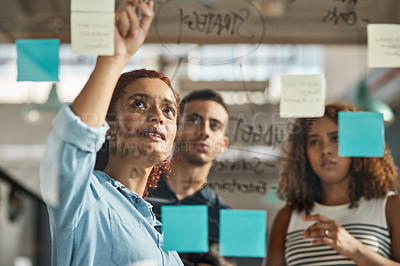 Buy stock photo Shot of a group of young designers brainstorming with notes on a glass wall in an office