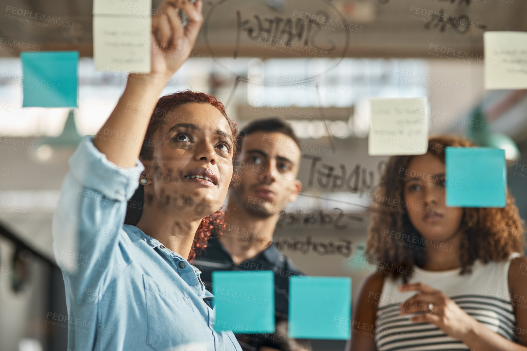 Buy stock photo Shot of a group of young designers brainstorming with notes on a glass wall in an office
