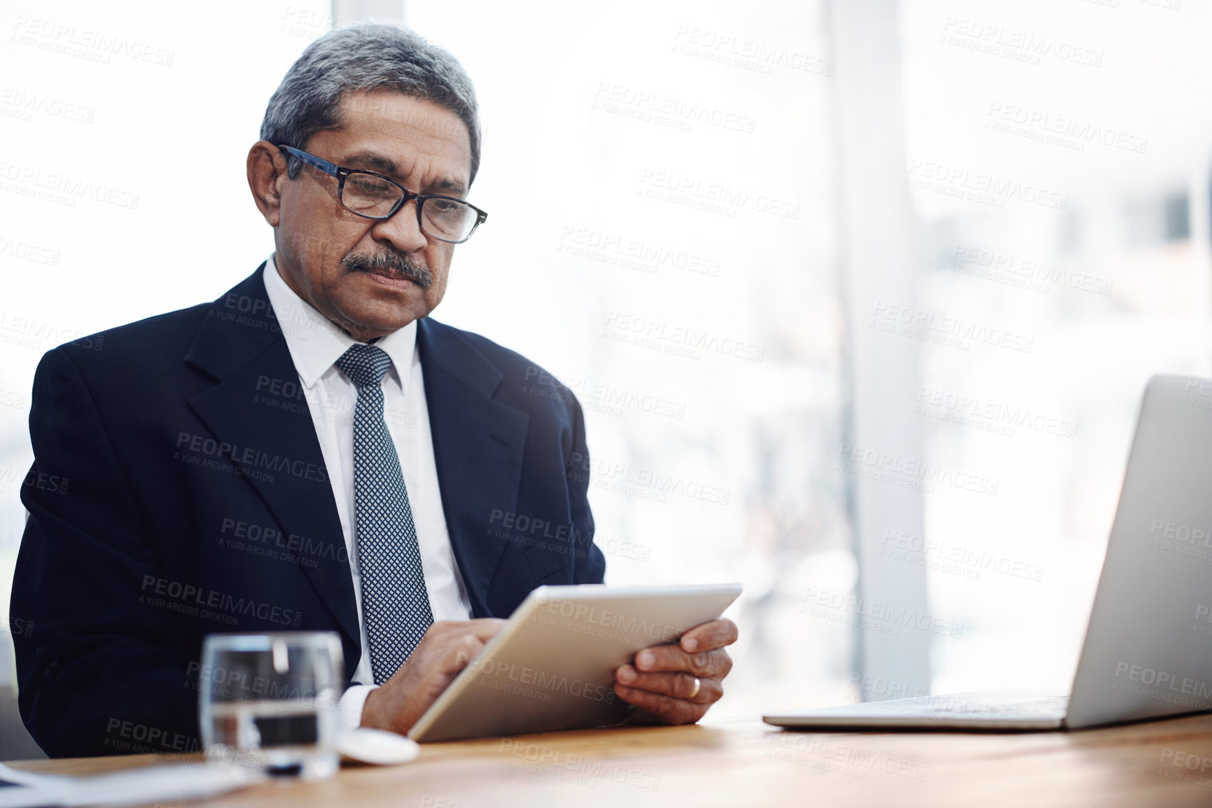 Buy stock photo Shot of a mature businessman working on a digital tablet in an office