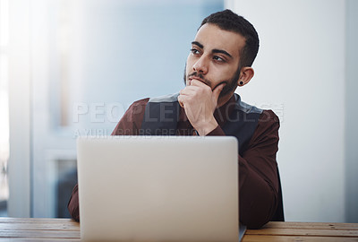 Buy stock photo Shot of a young businessman looking thoughtful while working on a laptop in an office