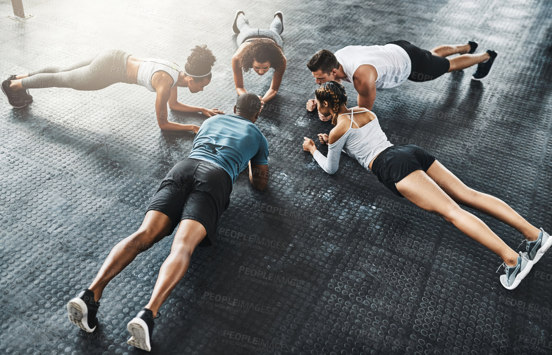 Buy stock photo Shot of a group of young people doing planks together during their workout in a gym