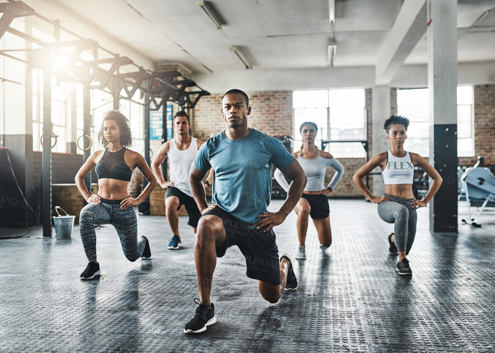 Buy stock photo Shot of a group of young people doing lunges together during their workout in a gym