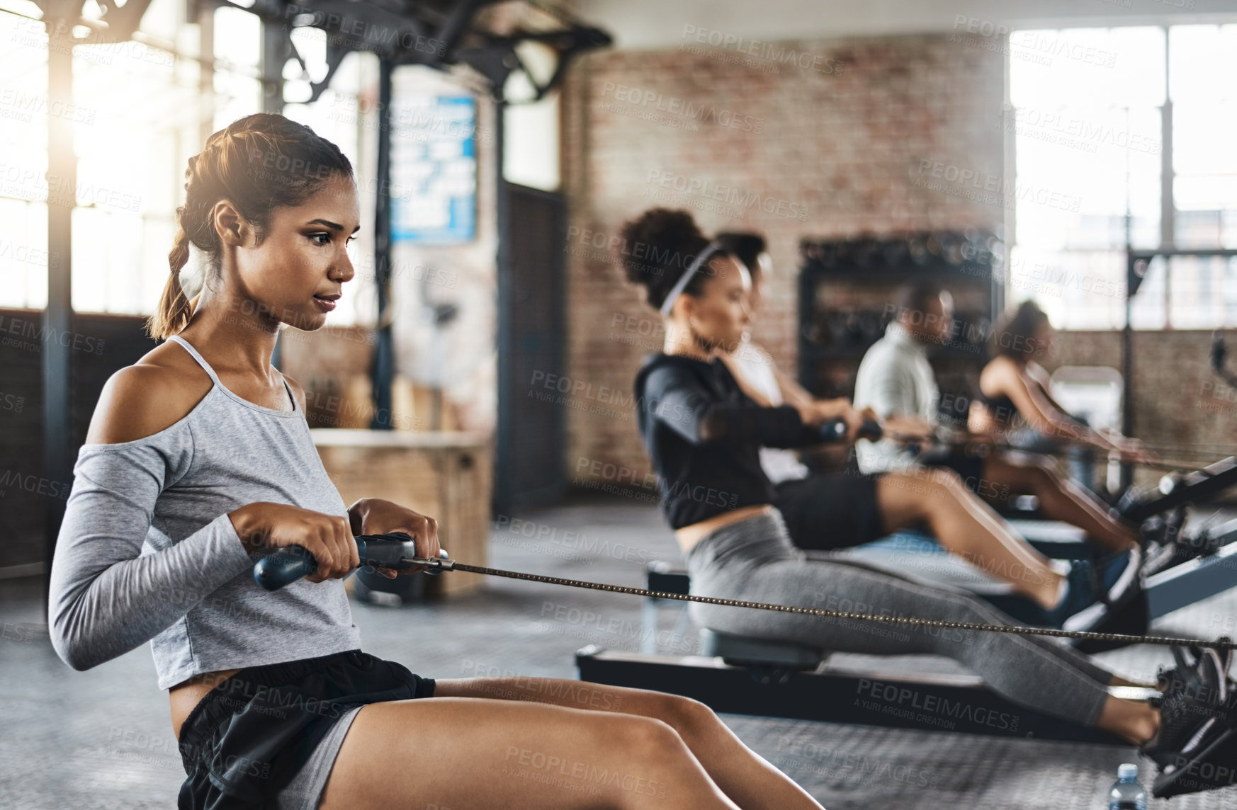 Buy stock photo Shot of a young woman working out with a rowing machine in the gym