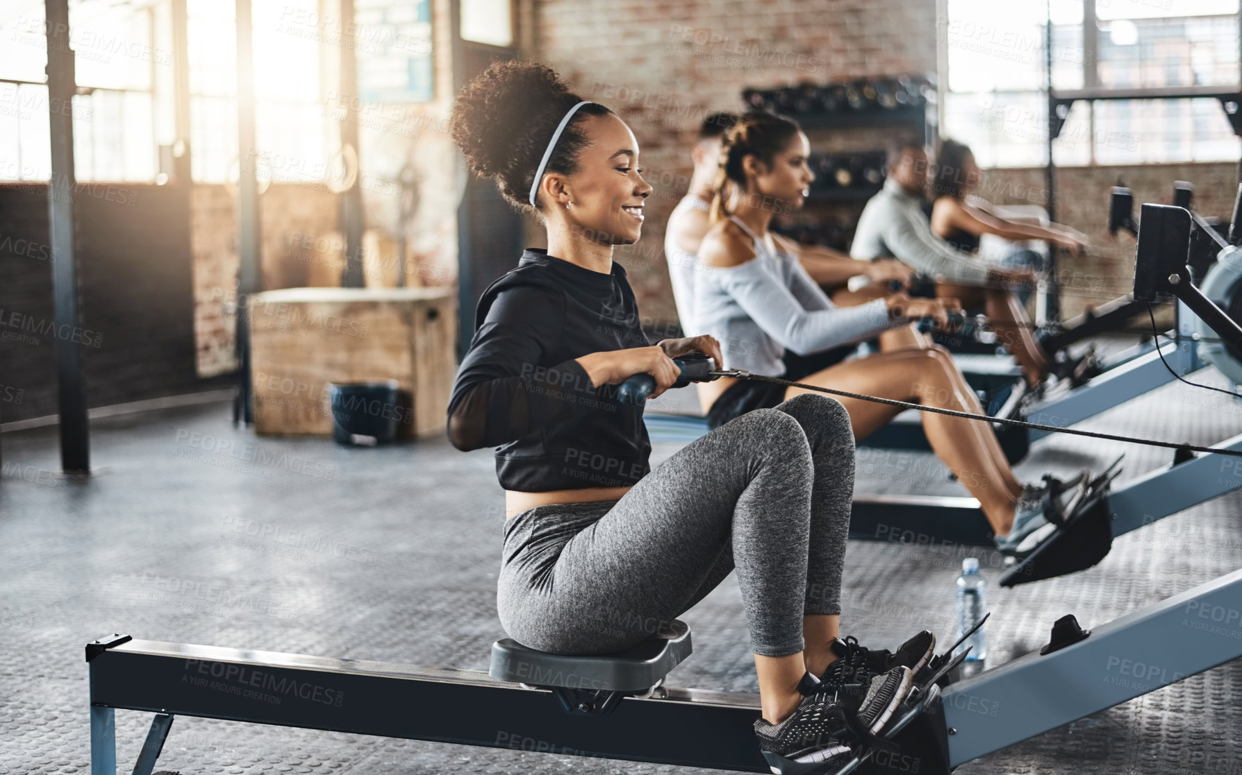 Buy stock photo Shot of a young woman working out with a rowing machine in the gym