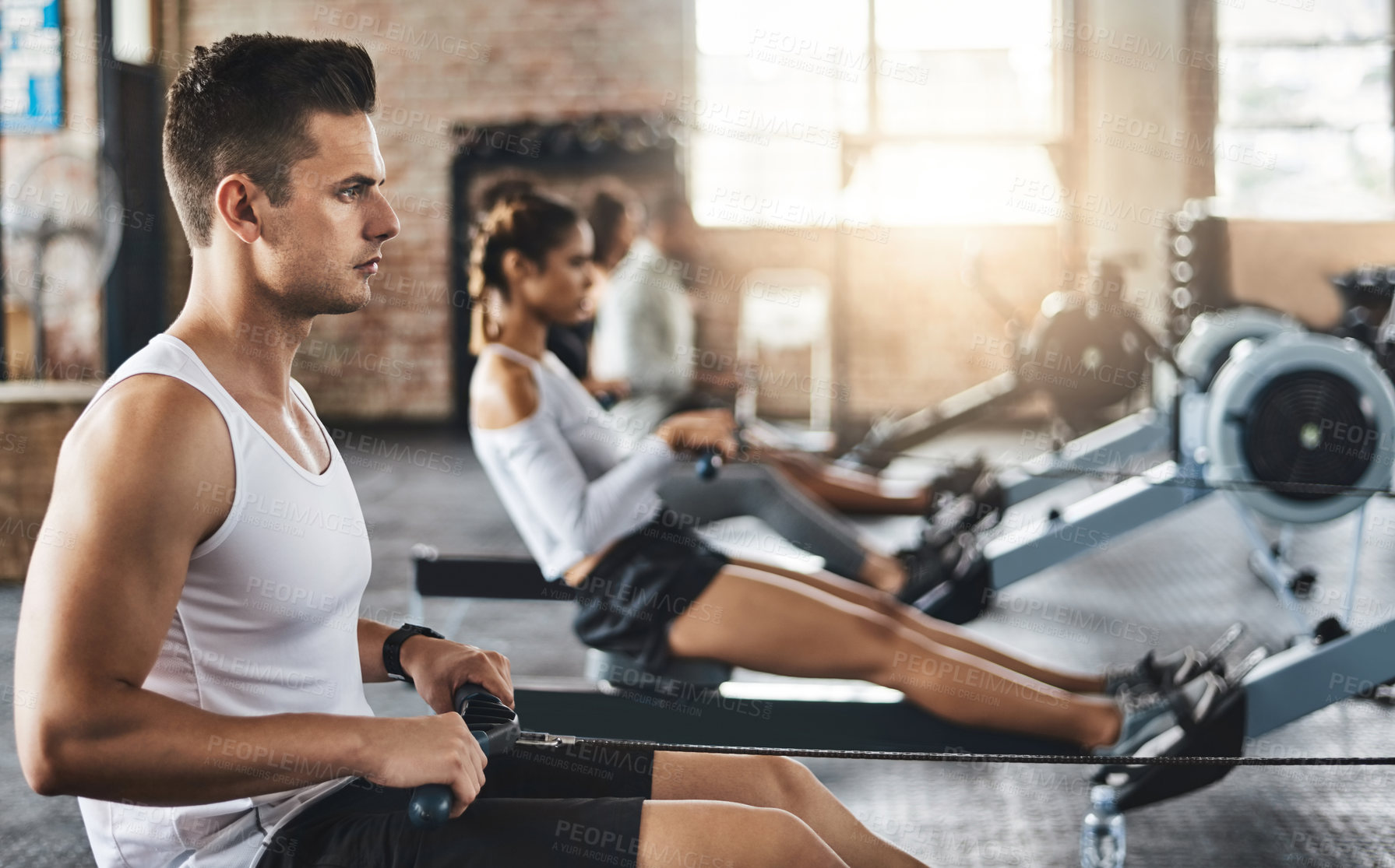 Buy stock photo Shot of a young man working out with a rowing machine in the gym