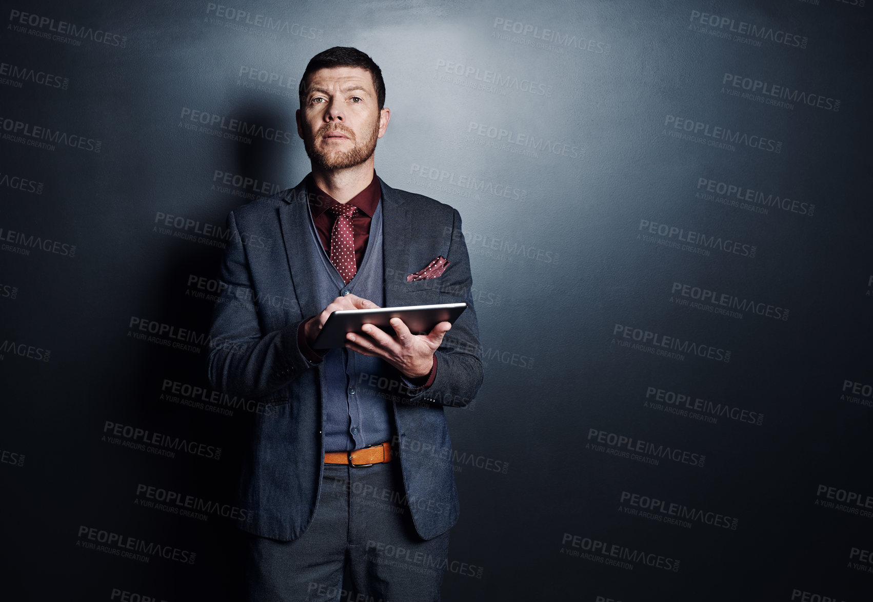 Buy stock photo Cropped shot of a handsome young businessman using his tablet while standing against a dark background
