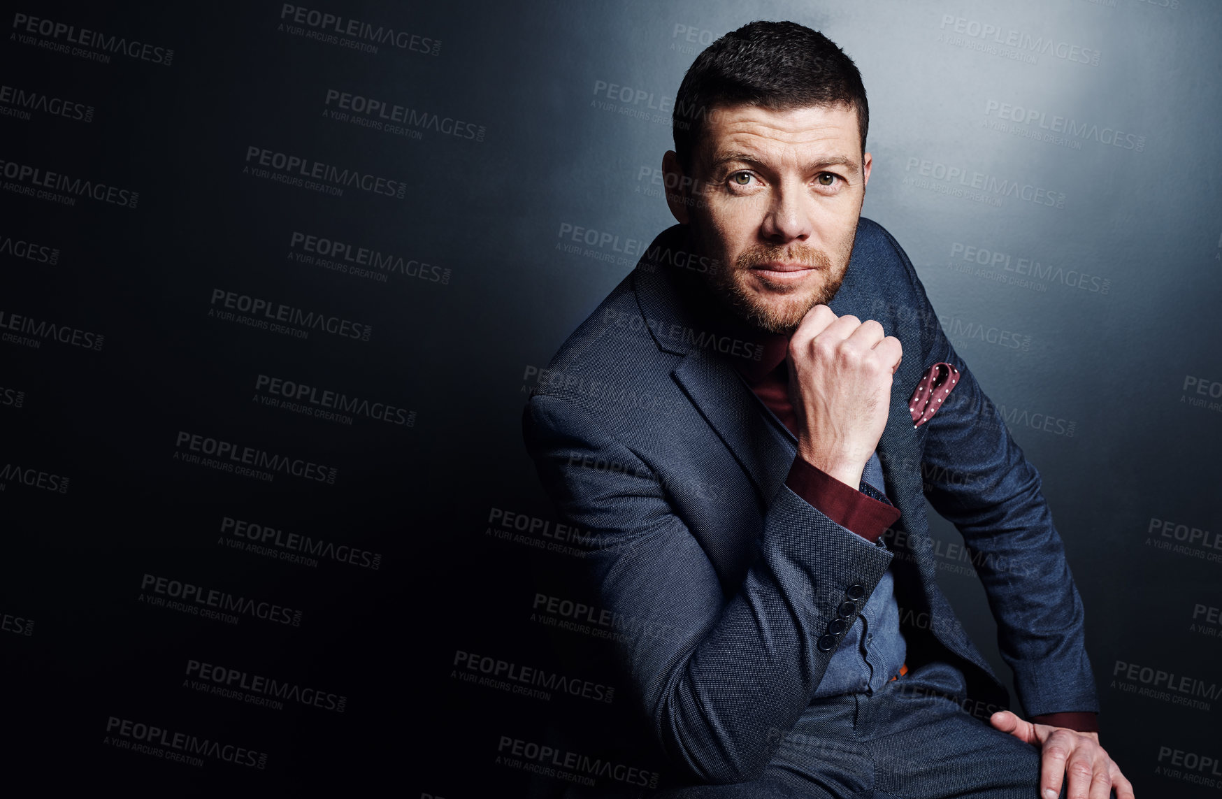 Buy stock photo Cropped portrait of a handsome young businessman sitting with his hand on his chin against a dark background