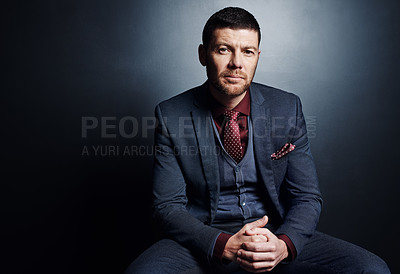Buy stock photo Cropped portrait of a handsome young businessman sitting in the studio against a dark background