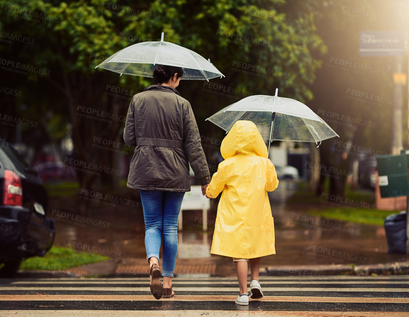 Buy stock photo Back, raincoat or umbrella with a mother and daughter walking across a street in the city during winter. Autumn, crosswalk or park with a woman and female child holding hands while crossing a road