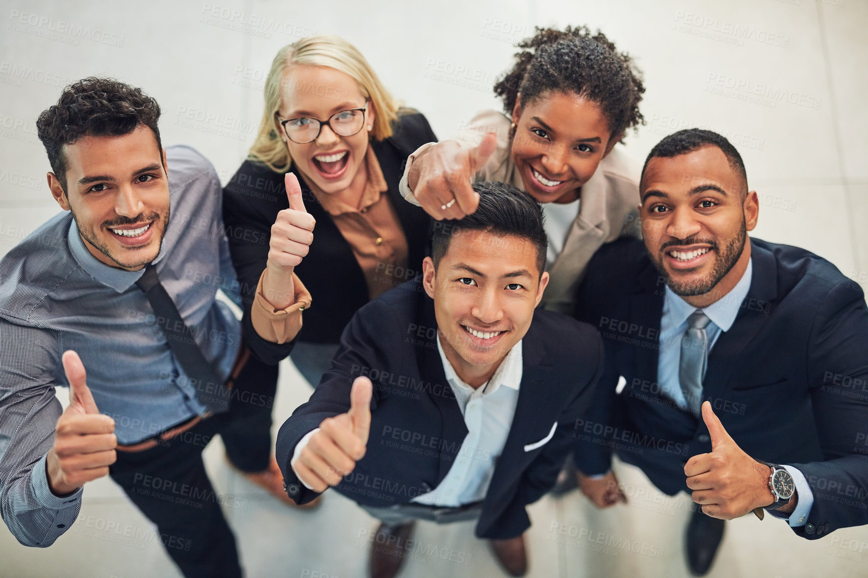 Buy stock photo High angle portrait of a group of cheerful young businesspeople showing thumbs up in the air while standing in the office during the day