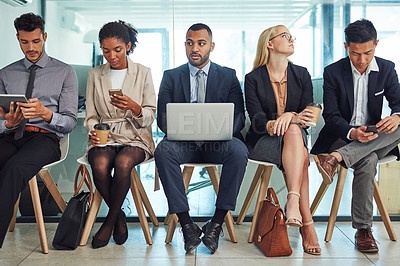 Buy stock photo Shot of a group of focussed young businesspeople seated together on chairs and making notes using different methods while waiting in the office during the day