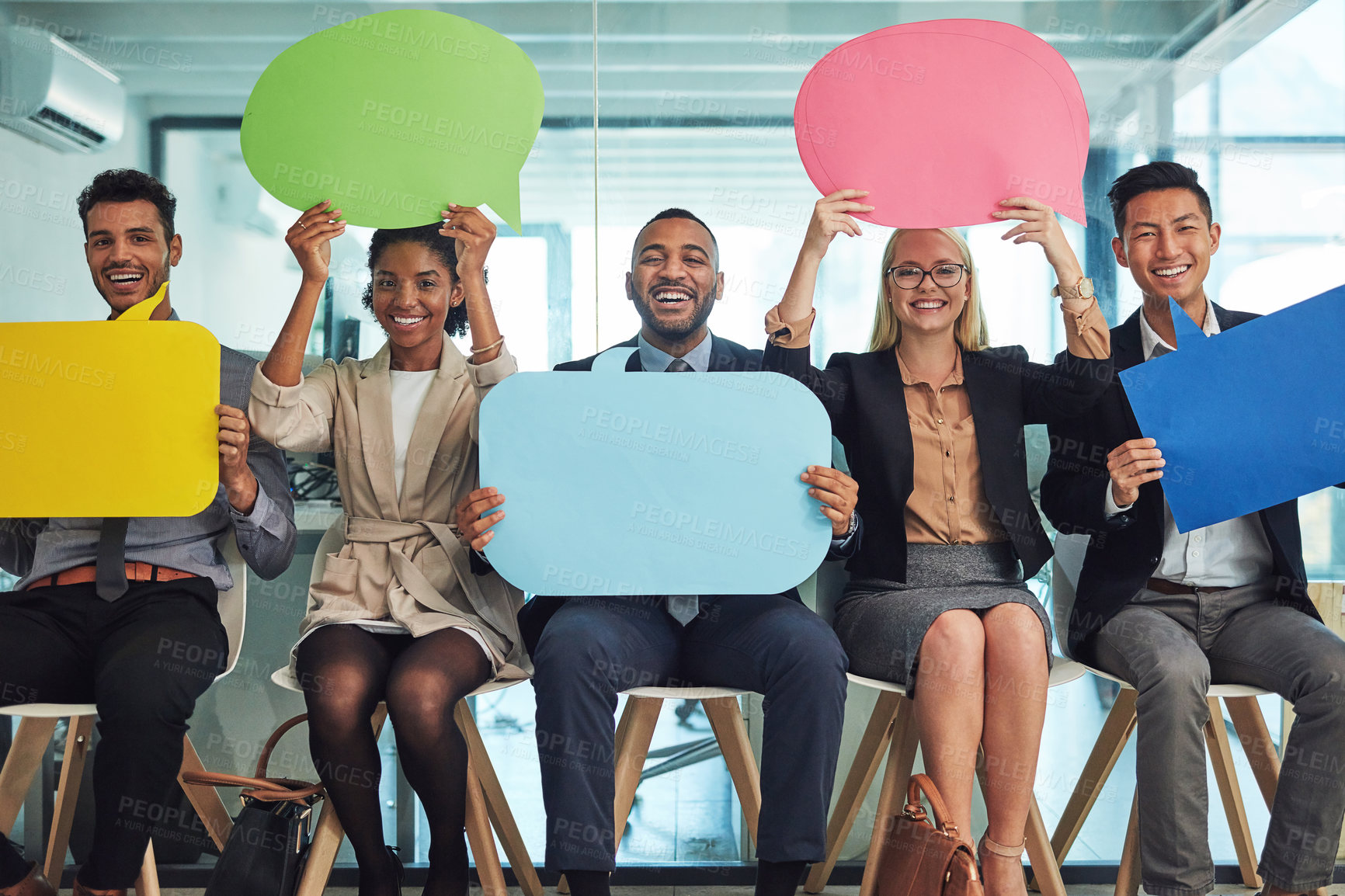 Buy stock photo Portrait of a group of cheerful young businesspeople seated together on chairs while holding up signs inside of the office during the day