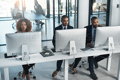 Buy stock photo High angle shot of three corporate businesspeople working on their computers in the office