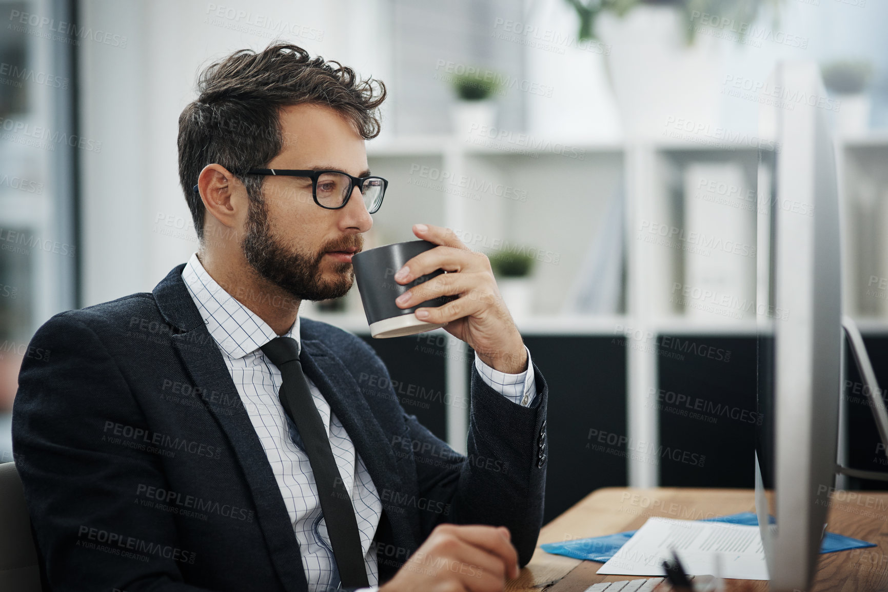 Buy stock photo Shot of a young businessman drinking coffee while working in an office